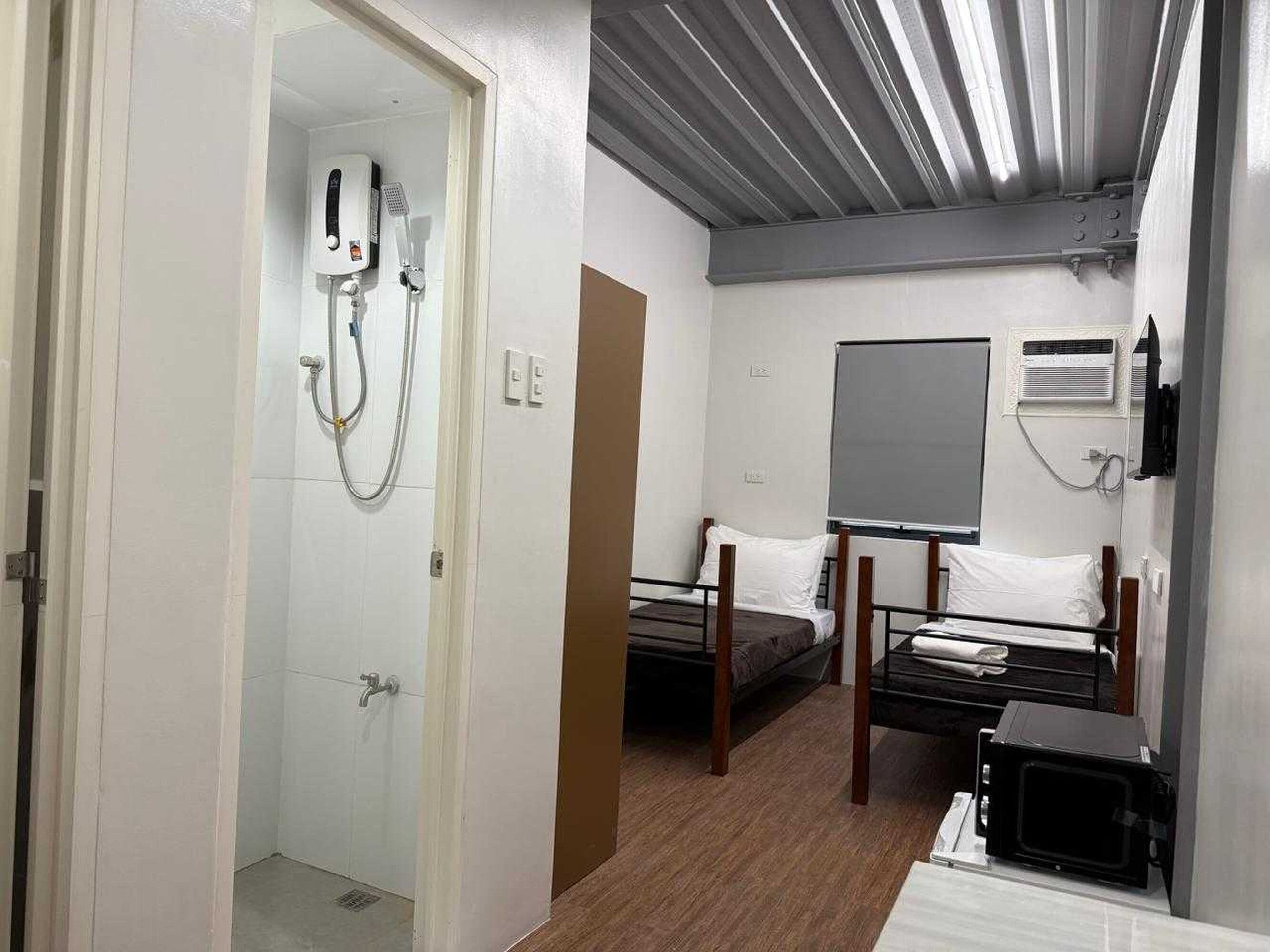 A compact hotel room with a shower, a bed, a bedside table, a microwave, and a large window.