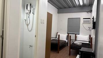 A compact hotel room with a shower, a bed, a bedside table, a microwave, and a large window.