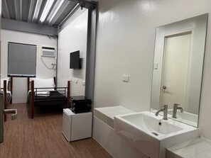 A hotel room with a bed, a small refrigerator, a white sink, a mirror, and a television on the wall. - Townhouse Oak Nexgen Apartments & Hotel (Pasay)