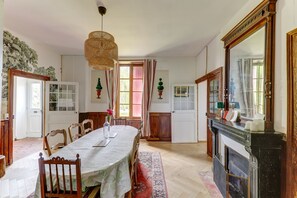 Une salle à manger avec une longue table, des chaises, une cheminée et un grand miroir.