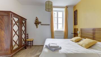 Un dormitorio con cama, un armario de madera, una silla, una ventana con cortinas y un aplique de pared.