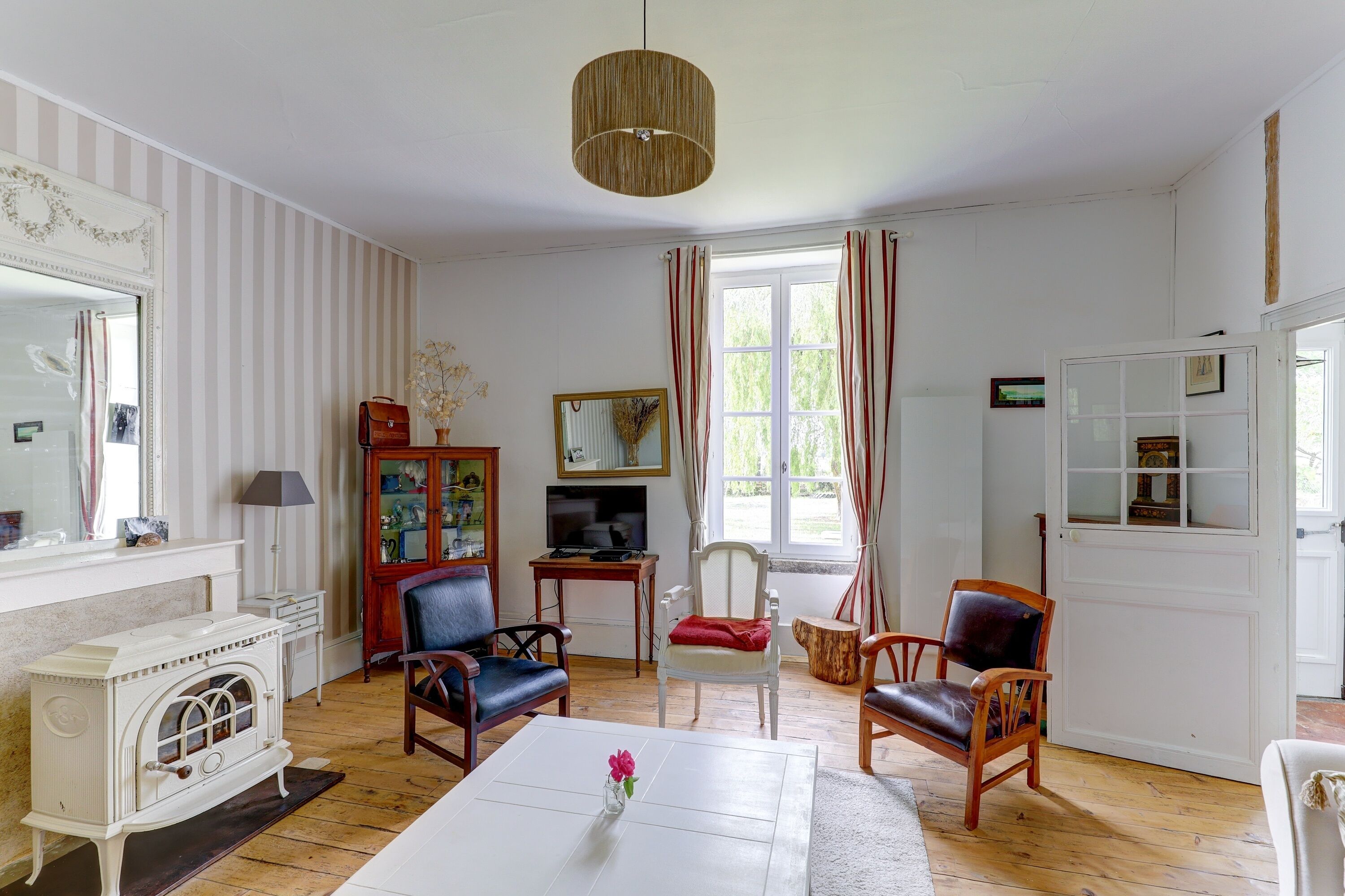 Una habitación con chimenea, televisor, mesa de comedor con un jarrón de flores y un ventanal con cortinas.