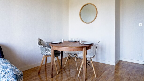 Een eethoek met een ronde houten tafel, vier stoelen en een spiegel aan de muur.
