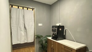 A small, well-lit room with a wooden cabinet, a water dispenser, a potted plant, and a shower curtain. - Muntri Inn by Soft Loft (George Town)