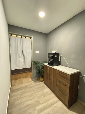 A small, well-lit room with a wooden cabinet, a water dispenser, a potted plant, and a shower curtain. - Muntri Inn by Soft Loft (George Town)