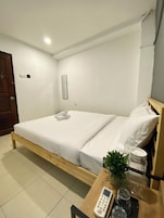 Habitación de hotel con una cama de madera, una mesita de noche con control remoto, vasos y una planta.
