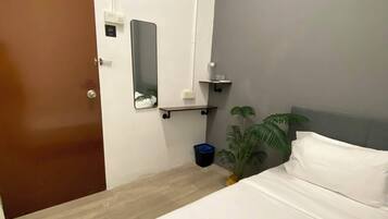 Habitación de hotel con cama, mesita de noche, espejo, equipo de aire acondicionado y puerta.