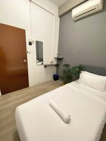 Habitación de hotel con cama, mesita de noche, espejo, equipo de aire acondicionado y puerta.
