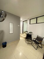 Una habitación con ventilador, una silla, un pequeño bote de basura y una escalera que lleva a otra zona.