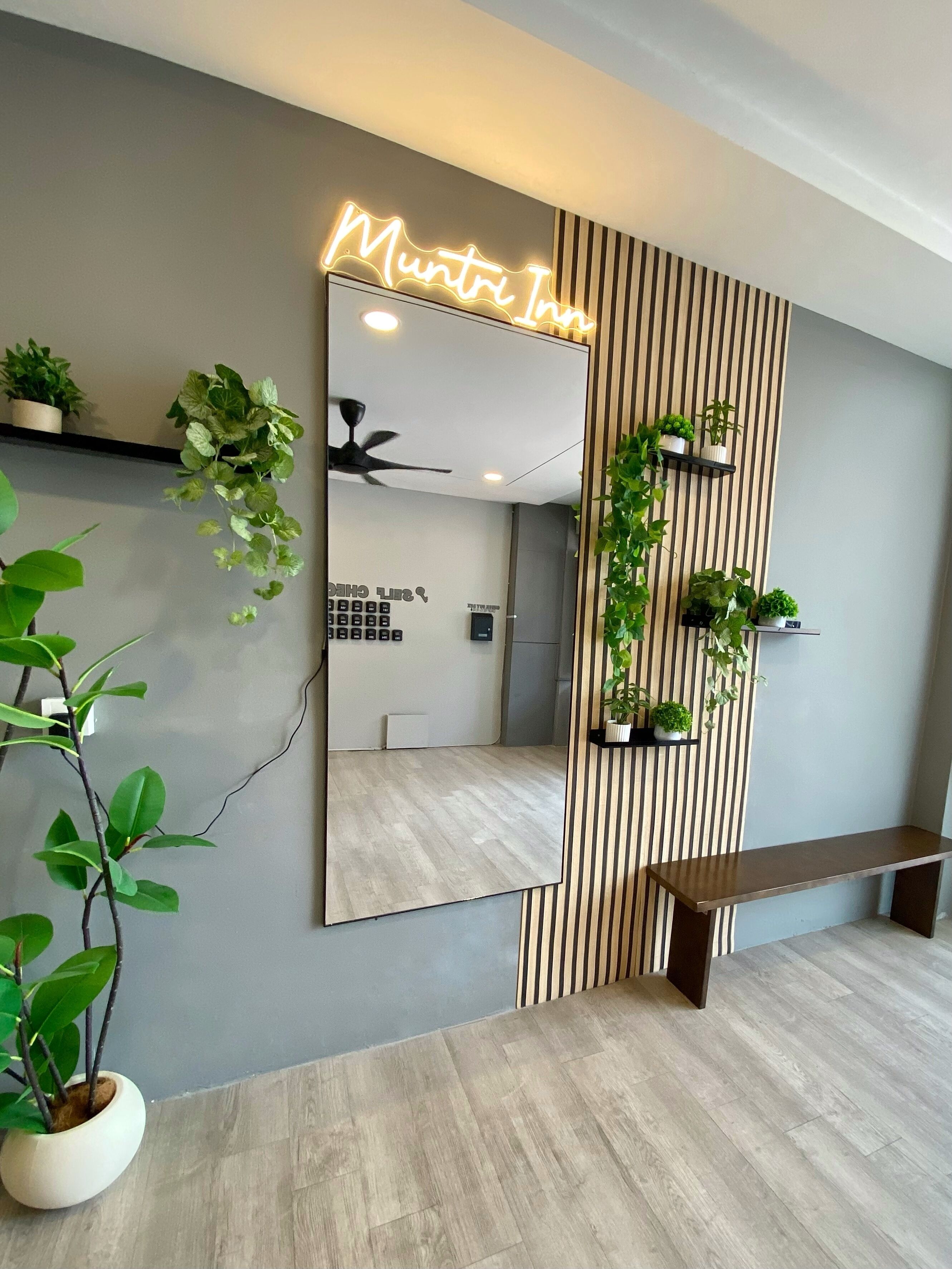 A hotel room with a large mirror, a ceiling fan, a wooden bench, and potted plants.
