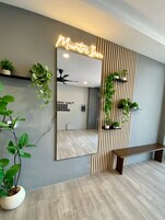 Una habitación de hotel con un espejo grande, un ventilador de techo, un banco de madera y plantas en macetas.
