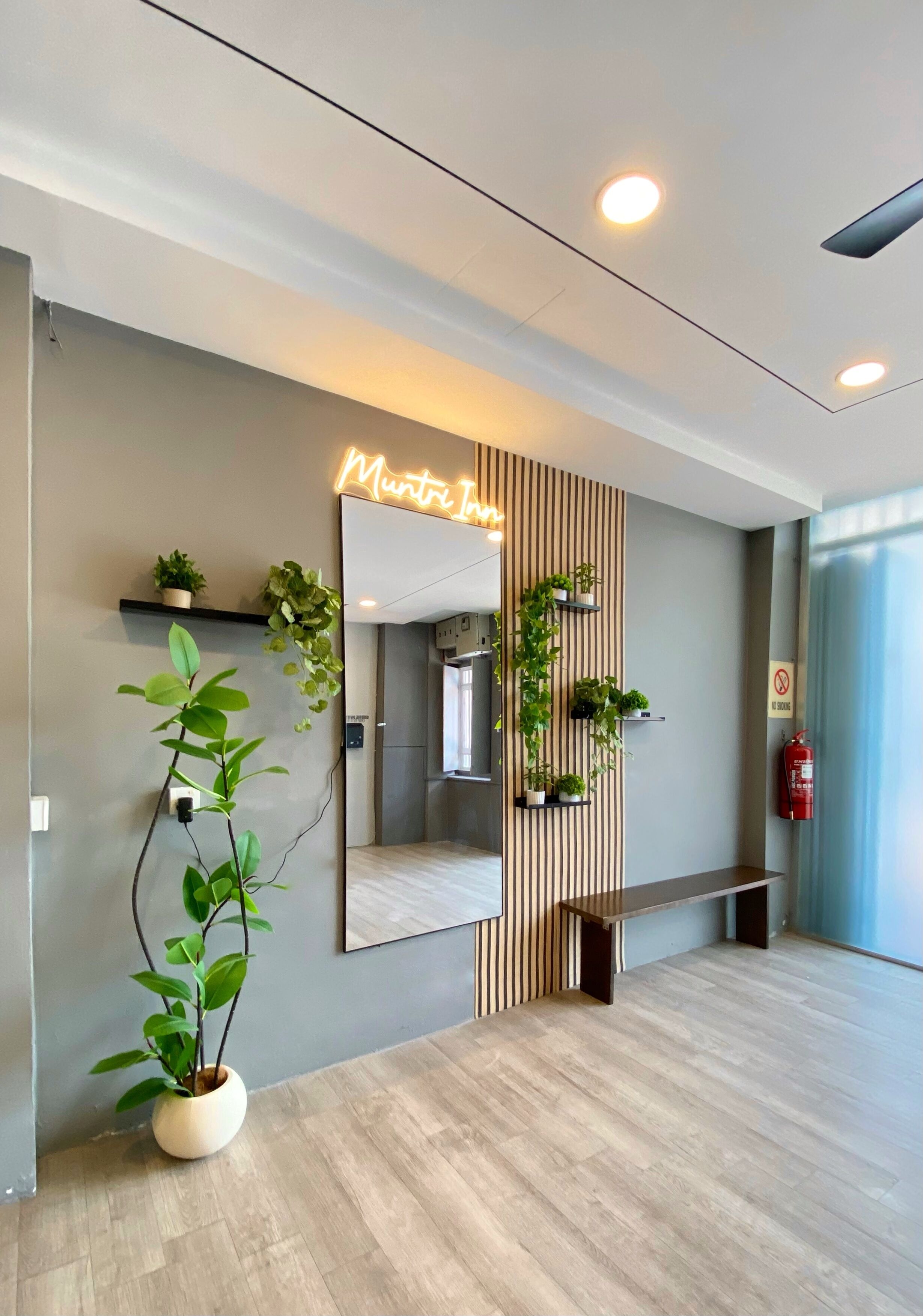 A modern reception area with a neon sign, a large mirror, vertical wooden slats, and potted plants.