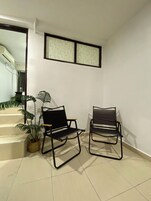 Una habitación con dos sillas de metal negro, una planta en maceta y una escalera que lleva a otra zona.