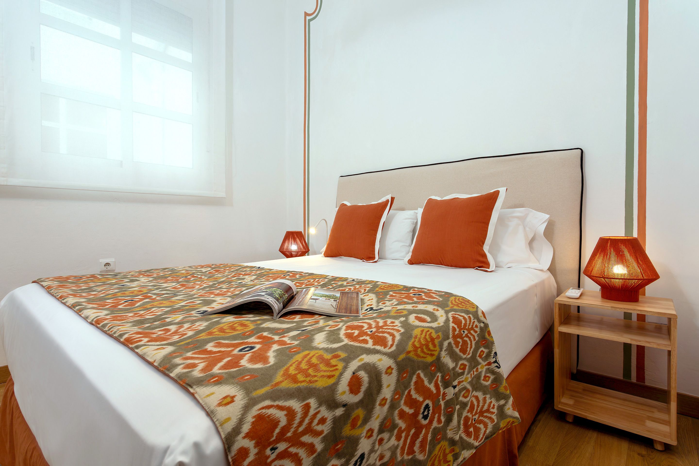 A neatly made bed with a patterned bedspread, a bedside lamp, and a book on the bed.