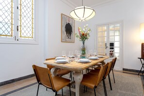 Ein Essbereich mit einem Holztisch, gedeckt für sechs Personen, umgeben von sechs Stühlen, einer Blumenvase und einem Bild an der Wand.
