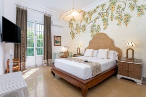 Ein Hotelzimmer mit einem großen Bett, einem Fernseher, einem Fenster mit Vorhängen, einer Wandlampe und einem dekorativen Wandbild.