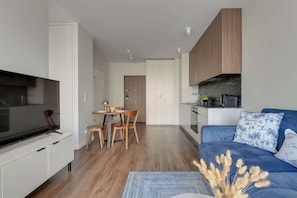 A modern living room with a flat-screen TV, a blue sofa with patterned cushions, and a dining area with wooden chairs and a small table. - Scala 16 | Parking | City Center (Gdańsk)