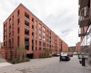 A multi-story brick building with balconies, a parking area, and a pedestrian walkway. - Scala 16 | Parking | City Center (Gdańsk)