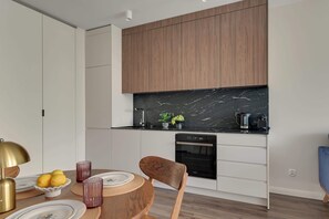 A modern kitchen with white cabinets, a black marble countertop, and a built-in oven. - Scala 16 | Parking | City Center (Gdańsk)