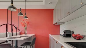 A compact kitchen with a red accent wall, a dining area with a white table and black chairs, and a coffee machine on the counter. - Rezydencja Wintera 1A | River View (Gdańsk)