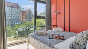 A bedroom with a large window, a bed with a grey blanket, and a red wall. - Rezydencja Wintera 1A | River View (Gdańsk)