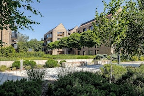 A modern residential building with multiple balconies, a landscaped garden area, and a clear blue sky.