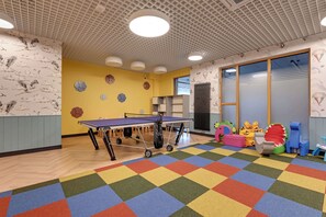 Ein Zimmer mit einem Pongtisch, farbenfrohem Teppich und verspielten Wanddekorationen.