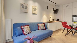 Ein modernes Wohnzimmer mit einem blauen Sofa, zwei dekorativen Kissen, einer Vase mit rosa Blumen und einem kleinen runden Tisch.