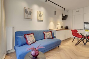 Ein modernes Wohnzimmer mit einem blauen Sofa, zwei dekorativen Kissen, einer Vase mit rosa Blumen und einem kleinen runden Tisch.