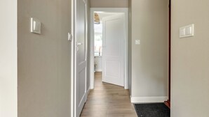 Een gang met witte muren, een houten vloer en een deur die naar een andere kamer leidt.