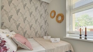 Een slaapkamer met een bed, kussens, een deken, een raam met luxaflex en wanddecoraties.