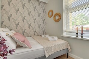 Ein Schlafzimmer mit einem Bett, Kissen, einer Decke, einem Fenster mit Jalousien und Wanddekorationen.