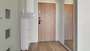 A hallway with a wooden door, a white wall-mounted phone, and a small white cabinet. - Nowa Motława B48 | Riverside | City Center (Gdańsk)