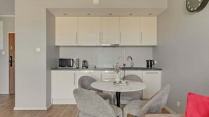 A modern kitchen with white cabinets, a round dining table, and grey upholstered chairs. - Nowa Motława B48 | Riverside | City Center (Gdańsk)