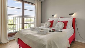 A bedroom with a large window, a bed with red and white bedding, and two wall-mounted lights. - Nowa Motława B48 | Riverside | City Center (Gdańsk)