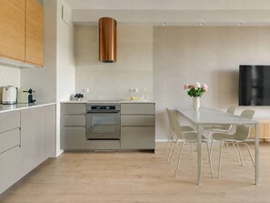 Eine moderne Küche mit Edelstahlgeräten, einer Messing-Dunstabzugshaube und einem Essbereich mit weißem Tisch und Stühlen.