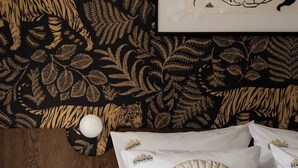 Un dormitorio con una cama, almohadas, una mesita de noche, una lámpara y una pared con un diseño de hojas.