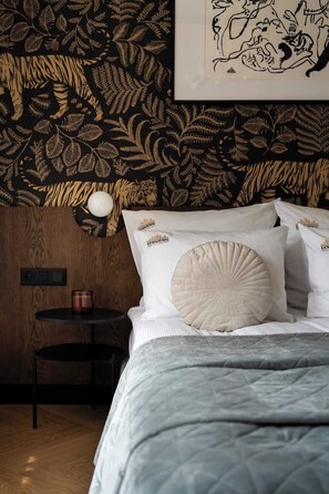 Ein Schlafzimmer mit einem Bett, Kissen, einem Nachttisch, einer Lampe und einer Wand mit einem Blattmuster.