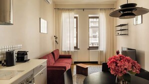 Un espacio habitable compacto con kitchenette, un sofá, una mesa de comedor con sillas y un jarrón con flores.