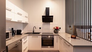 Een moderne keuken met witte kasten, een zwarte afzuigkap, een inbouwoven en een roestvrijstalen spoelbak.