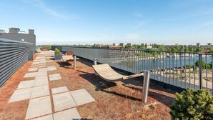 A rooftop terrace with a view of a river and cityscape, featuring a metal railing, a wooden deck, and a gravel path. - Chlebova 4.19 | Motława River & Shipyard | Gym (Gdańsk)