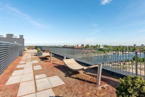 Eine Dachterrasse mit Blick auf einen Fluss und eine Stadtansicht, mit Metallgeländer, Holzdeck und Kiesweg.