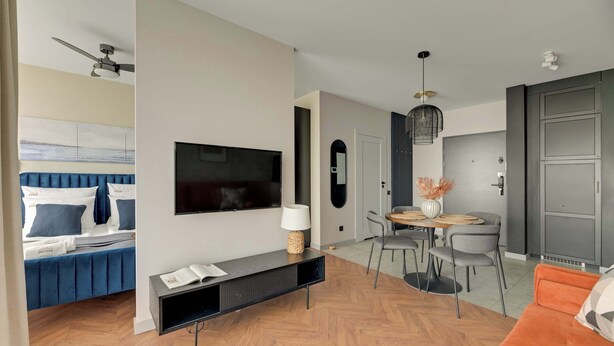 A modern living room with a flat-screen TV, a sofa, a dining table with chairs, and a kitchen area with cabinets. - Chlebova 4.19 | Motława River & Shipyard | Gym (Gdańsk)