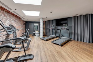 Ein Fitnessraum mit Laufbändern, Ergometer und einer Backsteinwand.