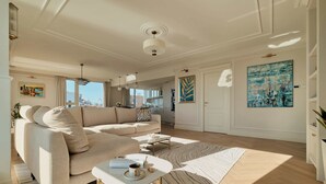 Una sala de estar moderna con un sofá color beige, una mesa de centro y vistas de la ciudad a través de amplias ventanas.