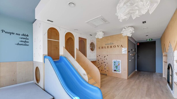 Zona de juegos infantiles con un tobogán, una pared con un letrero sobre juegos y una estructura de madera para jugar.