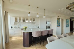 A modern kitchen with marble countertops, a central island with bar stools, and pendant lighting. - 140sqm | Chlebova Penthouse | Riverview | Parking (Gdańsk)