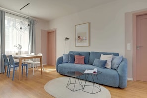 A modern living room with a blue sofa, a dining table with chairs, a coffee table, and a pendant light.