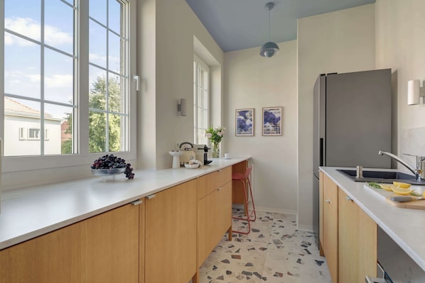 A modern kitchen with large windows, a refrigerator, and a sink.