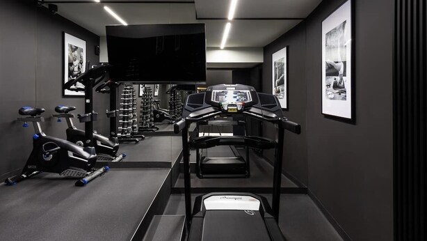 Et fitnessrum med træningsudstyr, løbebånd og et tv-skærm.
